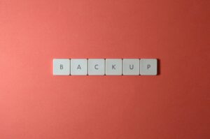 Free Close-up of keyboard keys spelling 'BACKUP' placed on a coral-colored surface. Stock Photo