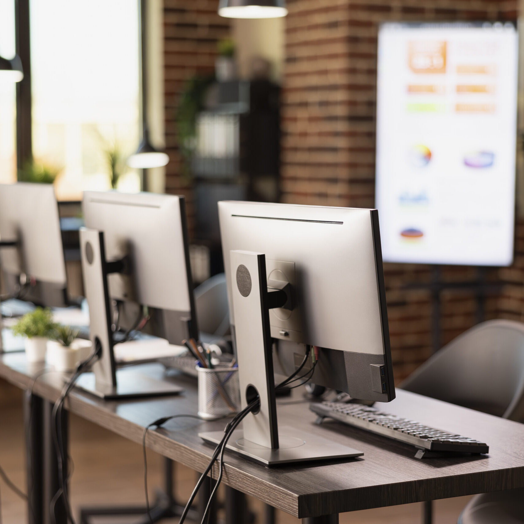 Vacant and organized brick wall office featuring a table and digital equipment for startup company. Empty modern workspace that is well arranged with multiple computers, ready for employees.